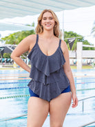 Woman wearing a navy blue swimsuit with ruffled details by a pool.