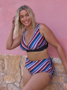 Woman wearing a colorful striped bikini against a pink wall.