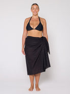 Woman wearing a black bikini and black sarong on a white background