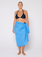 Woman wearing a black bikini top and blue sarong on a white background