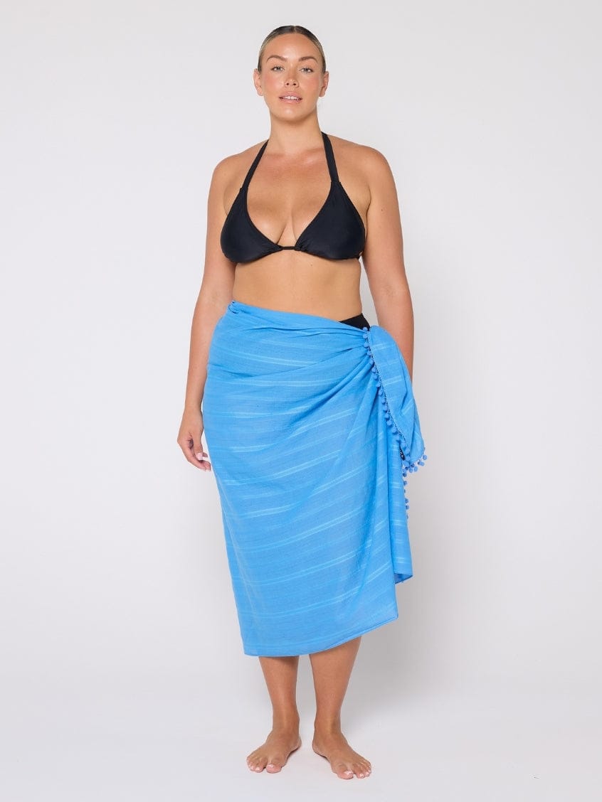 Woman wearing a black bikini top and blue sarong on a white background