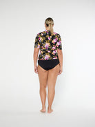 Person wearing a floral rash guard and black shorts on a white background