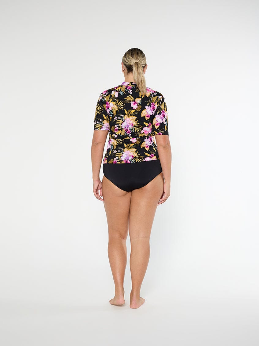 Person wearing a floral rash guard and black shorts on a white background