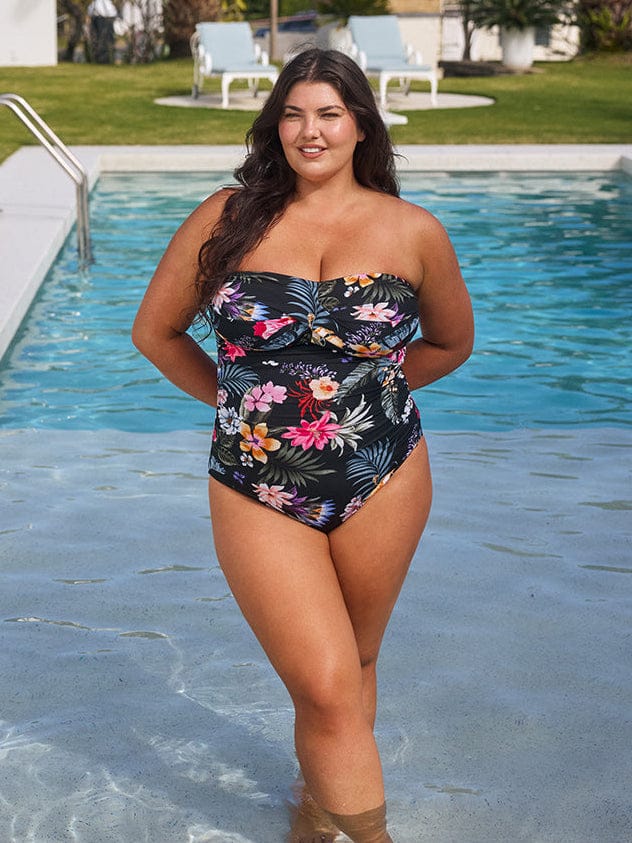 Woman in a floral swimsuit standing by a pool with greenery in the background