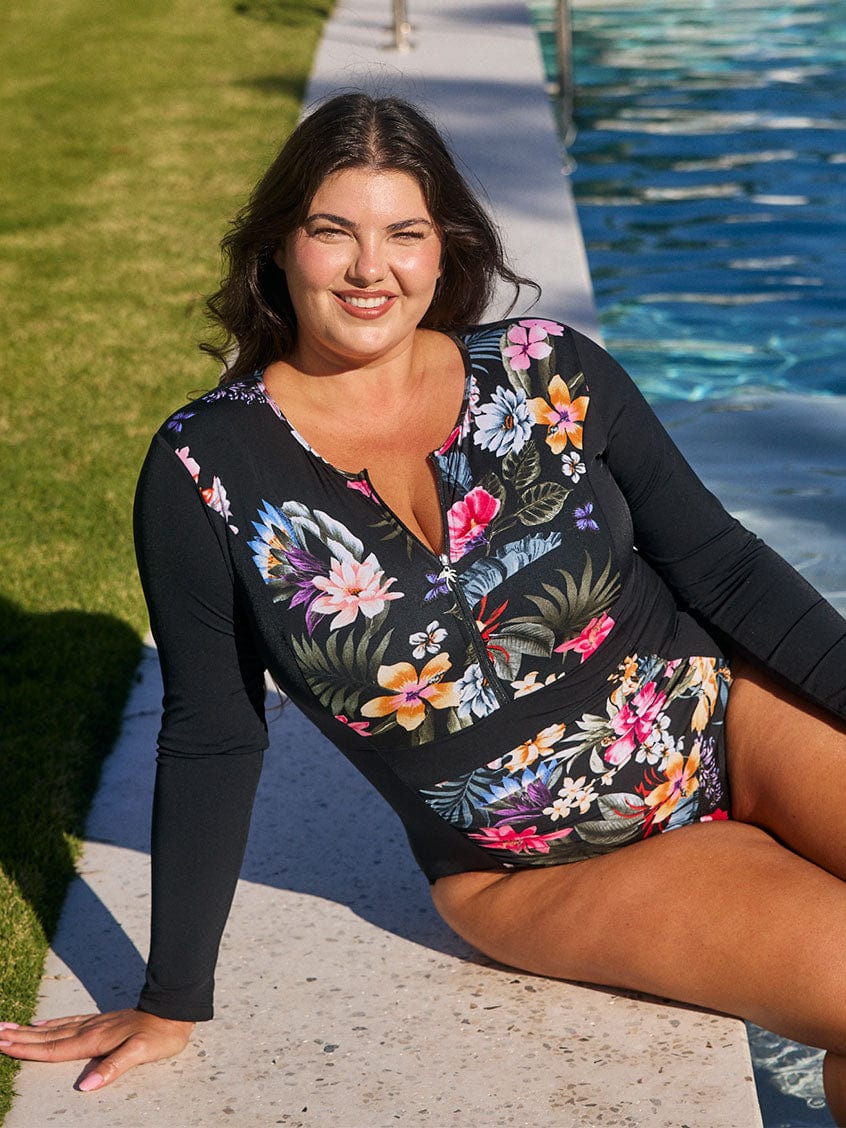 Brunette model wears flattering pool proof long sleeve one piece in black floral print
