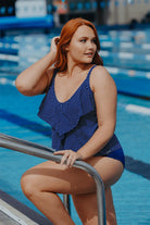 redhead model emerges from a pool wearing a navy ruffled swimsuit, the tankini is decorated with white dots and has frills down the front.