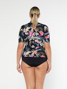 Blonde model shows the back of chlorine resistant floral short sleeve rash vest