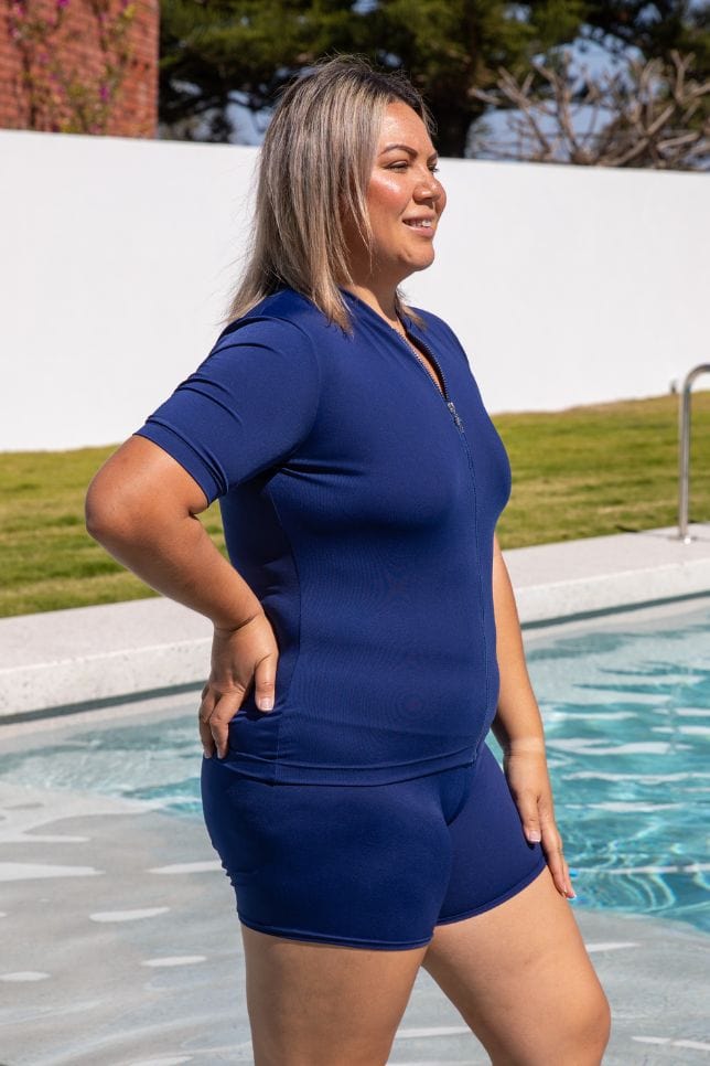 Blonde model standing in pool wearing modest chlorine resistant rash vest with zip front detail