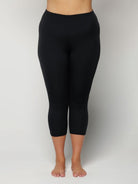 Woman wearing black capri leggings on a plain background