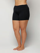 Woman wearing black swim shorts on a plain background