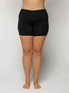 Woman wearing black swim shorts on a plain background