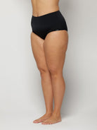 Woman wearing black high-waisted underwear on a plain background