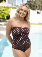 Woman wearing a brown strapless swimsuit with white polka dots by a pool.