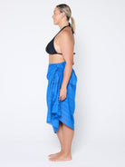 Woman wearing a black bikini top and blue sarong on a white background