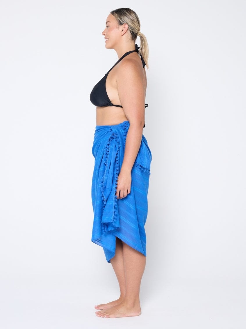 Woman wearing a black bikini top and blue sarong on a white background
