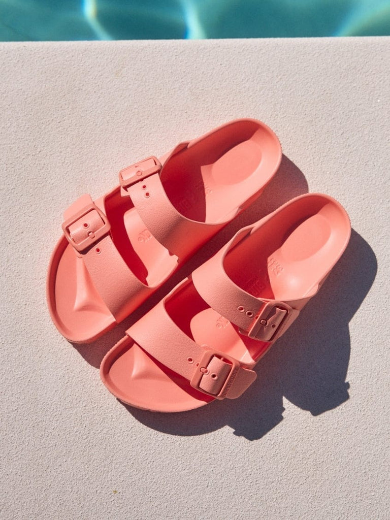 Pair of pink sandals on a diving board with a pool in the background
