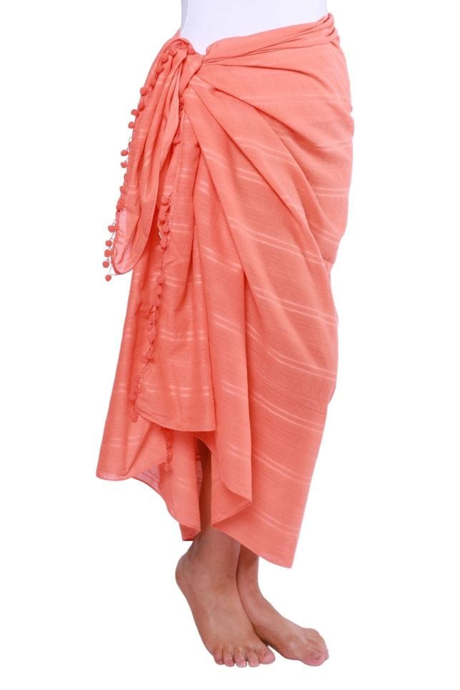 side profile of model wearing a coral cotton sarong tied to the side with pompom detail