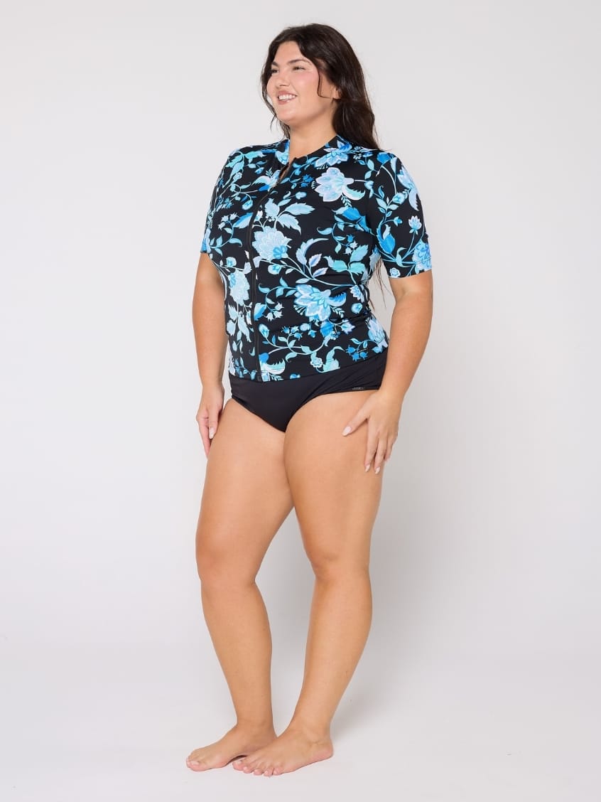 Woman wearing a black floral rash guard and black swimsuit bottoms on a white background