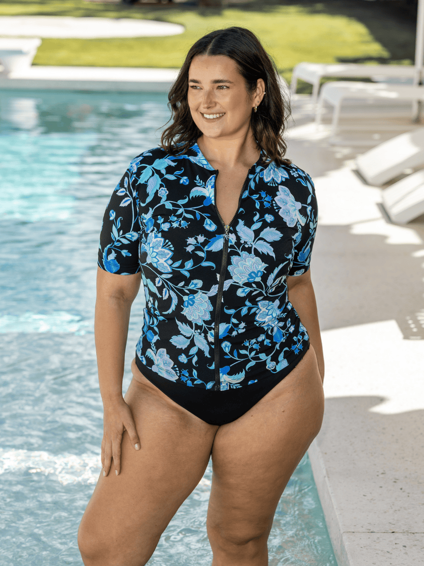 Woman wearing a black and blue floral rash vest in chlorine resistant by a pool