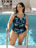 Woman in a black swimsuit with blue floral patterns standing by a pool.