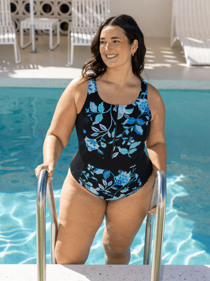 Woman in a black swimsuit with blue floral patterns standing by a pool.