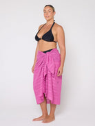 Woman wearing a black bikini top and pink sarong on a white background