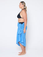 Woman wearing a black bikini top and blue sarong on a white background