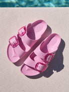 Pink sandals with buckles on a diving board near a pool.