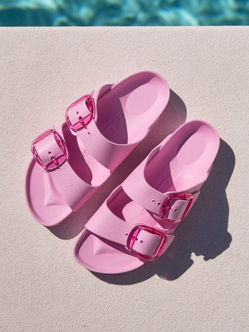 Pink sandals with buckles on a diving board near a pool.