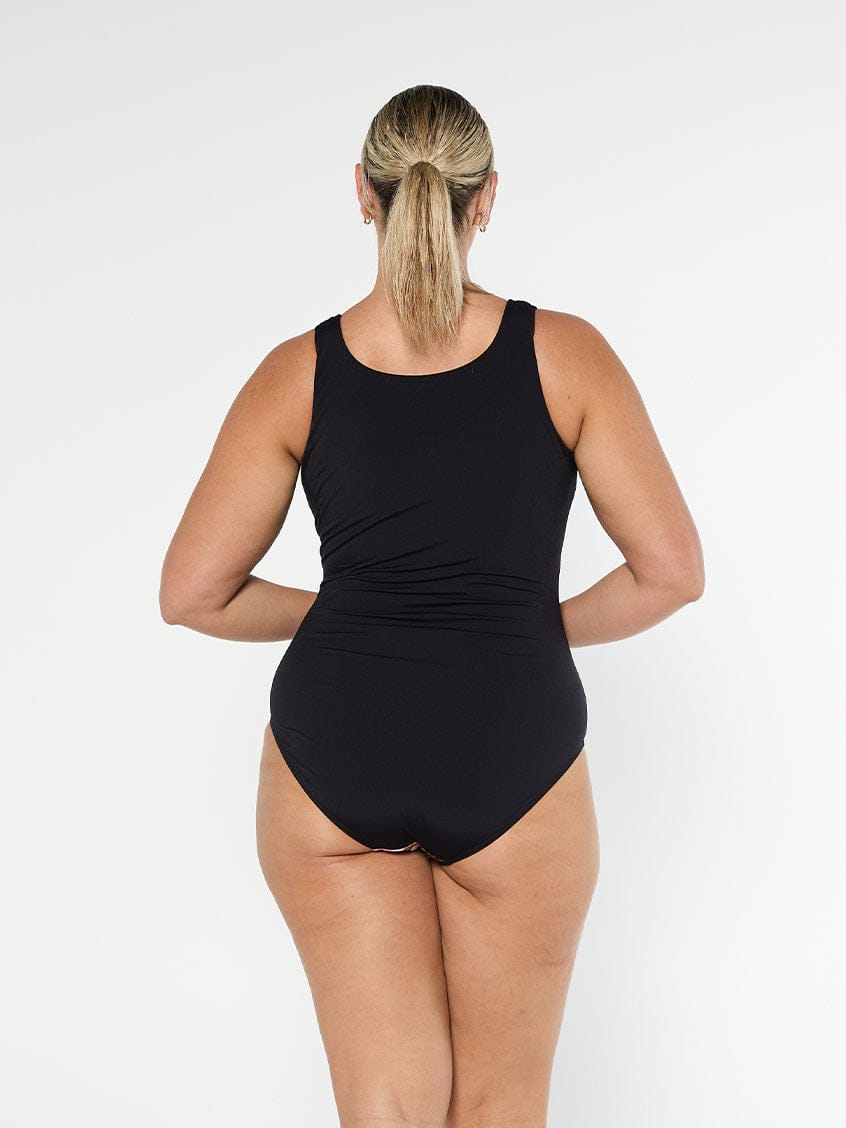 Blonde model wears black floral chlorine resistant sleeveless one piece with full coverage bottom and high back
