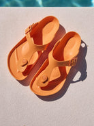 Pair of orange sandals on a diving board with a pool in the background
