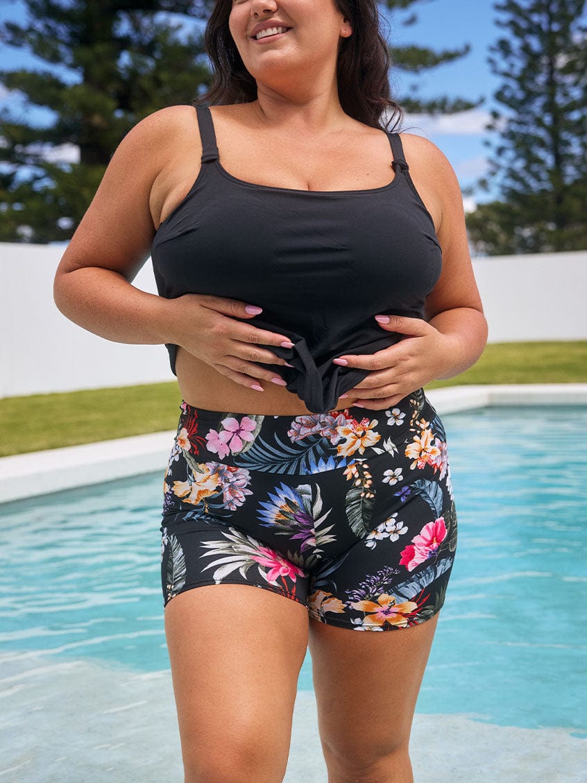 Brunette model wears black floral chlorine resistant high-waisted boyleg swim shorts