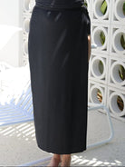 lady standing in front of a white walling wearing a long split swim skirt in black 