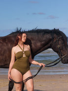 model stands next to a horse wearing figure flattering olive bandeau halter neck one piece with removable straps and power mesh front