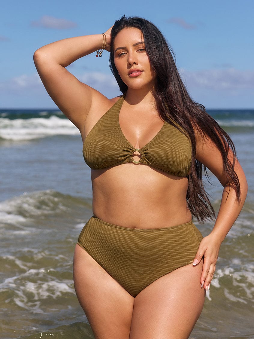 Woman in an olive green bikini standing on a beach with ocean waves in the background