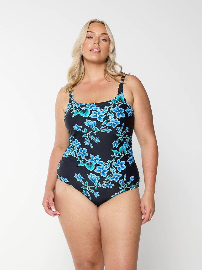 Blonde model shows blue floral swimsuit with scoop neckline and adjustable straps