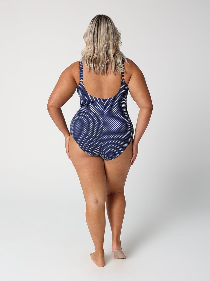 Person wearing a navy polka dot swimsuit on a white background