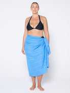 Woman wearing a black bikini top and blue sarong on a white background
