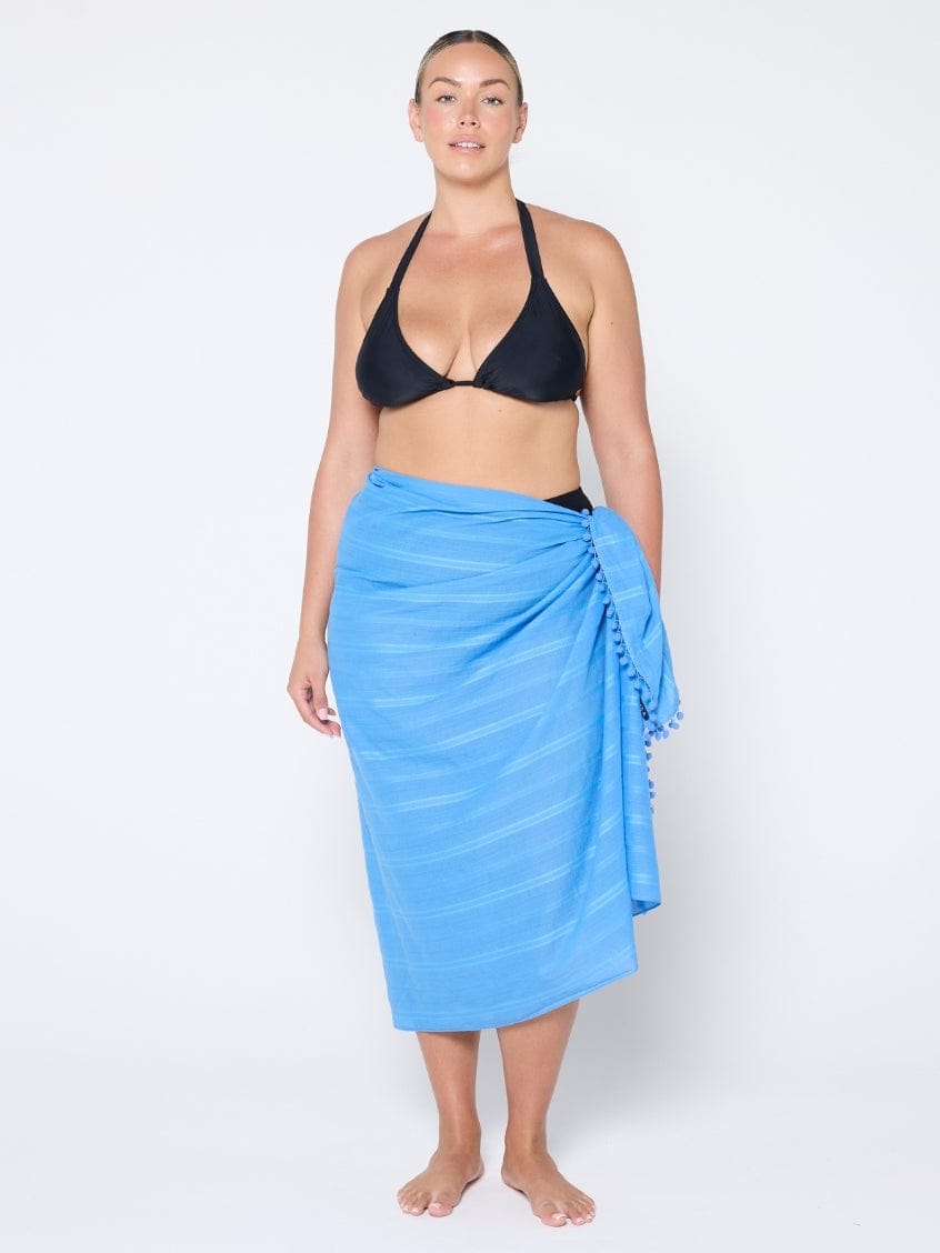 Woman wearing a black bikini top and blue sarong on a white background