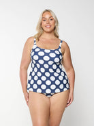 Blonde model shows the front of a flattering scoop neck tankini top with a navy and white polkadot pattern