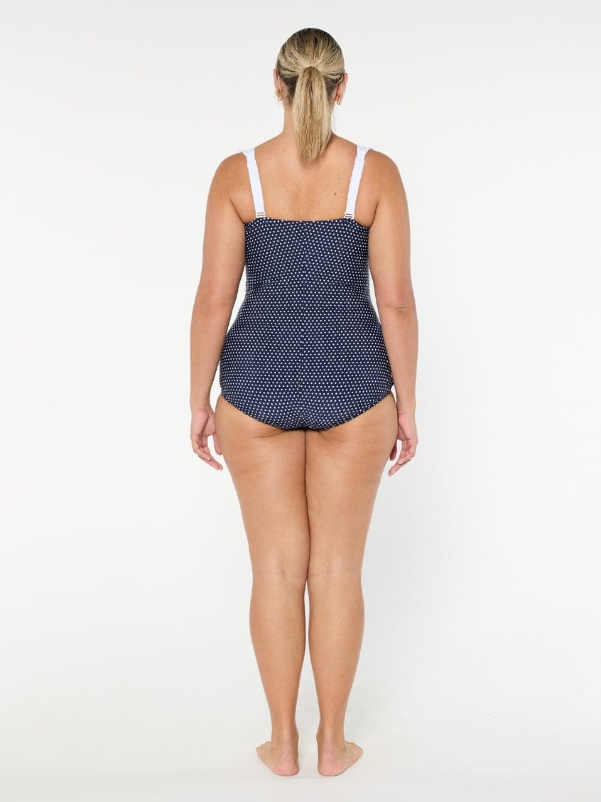 Woman wearing a navy polka dot swimsuit on a white background