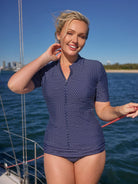 Woman wearing a blue polka dot swimsuit on a boat with water and sky in the background