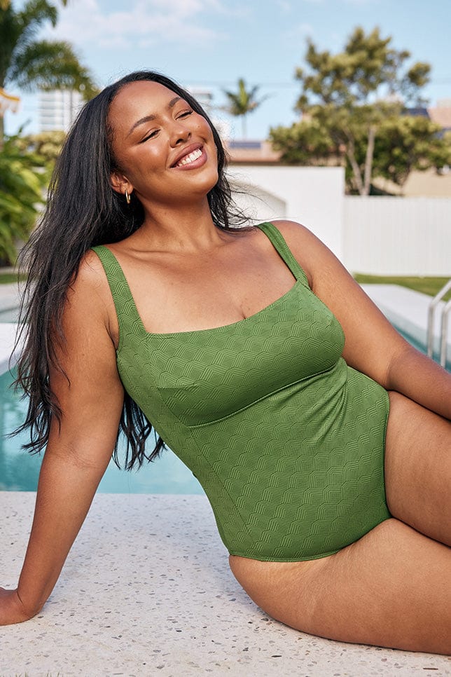 Model wearing green square neck one piece sitting near pool