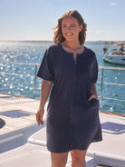Woman in a navy blue dress standing on a boat with water and sky in the background