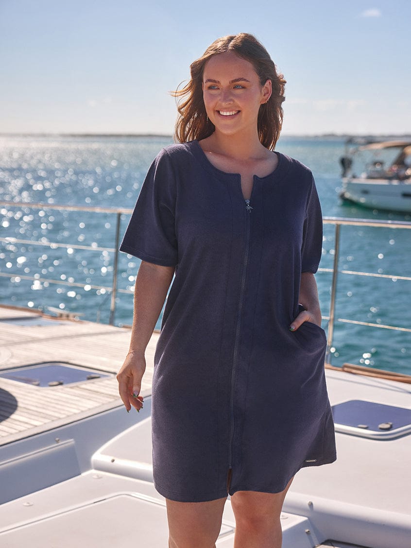 Woman in a navy blue dress standing on a boat with water and sky in the background