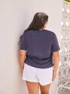 Person wearing a dark blue t-shirt and white shorts standing against a light-colored wall.