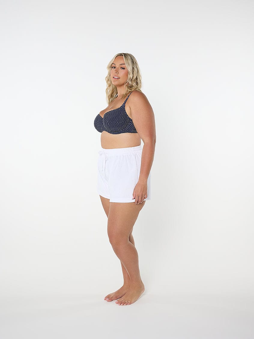 Woman wearing a navy patterned bikini top and white shorts on a white background