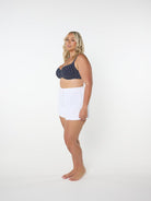 Woman wearing a navy patterned bikini top and white shorts on a white background