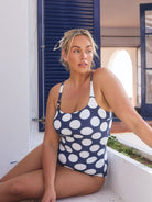 Blonde model wears navy and large white polka dot swimsuit with flattering scoop neckline