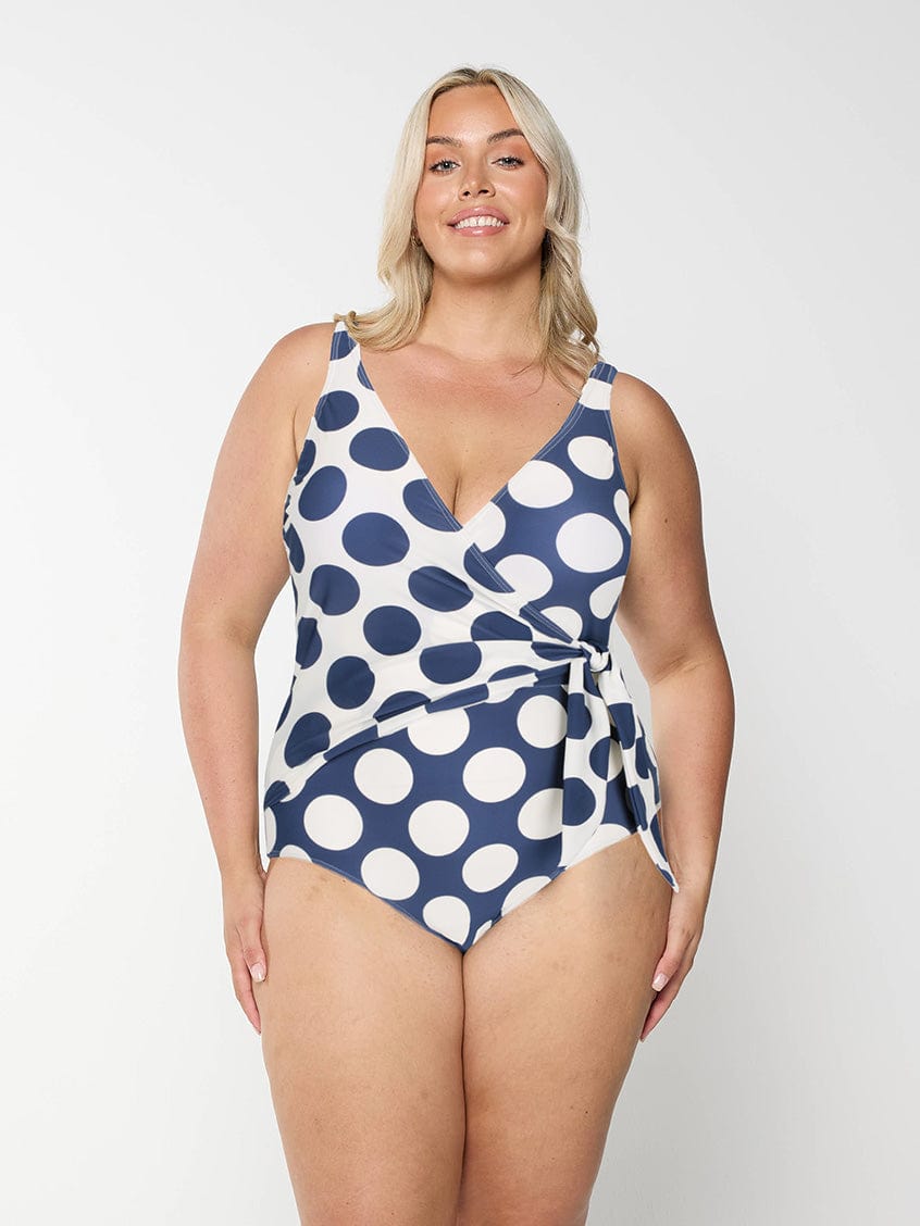 Woman wearing a blue and white polka dot swimsuit on a plain background